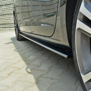 Close-up of a black car's side showing a chrome side skirt and low ground clearance beside a paved surface, wheel in view outside the frame.