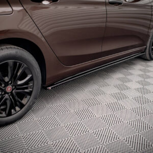 Close-up of a brown car's side panel and wheels, parked on a patterned showroom floor.