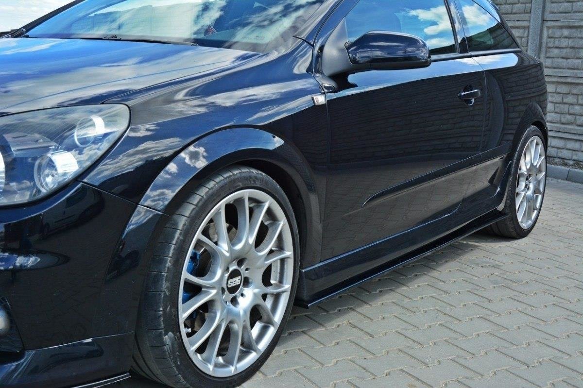 pol_po_SIDE-SKIRTS-DIFFUSERS-suitable-for-Opel-ASTRA-H-FOR-OPC-VXR-238_3jpg - OPSHOLDERS Close-up of a black sporty car showing its front side, glossy paint, and silver multi-spoke alloy wheels on a brick driveway.