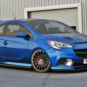 Blue modified hatchback with a lowered stance and large multi-spoke wheels parked in front of a corrugated metal building.