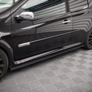 Close-up of a glossy black car side with door handle and rear wheel on a patterned showroom floor, reflecting light.