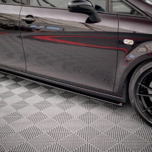 Close-up side view of a glossy black sports car showing the door, mirror, and wheel with red brake calipers on a patterned floor.