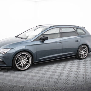 Gray station wagon-style car shown from the front-left side in a studio, with chrome alloy wheels and roof rails, on a checkered floor.