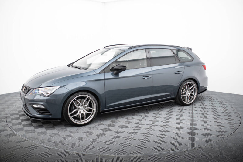 Gray station wagon-style car shown from the front-left side in a studio, with chrome alloy wheels and roof rails, on a checkered floor.