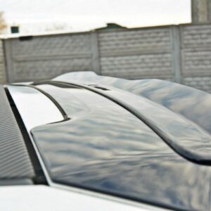 Close-up of a car's glossy rear spoiler with carbon-fiber texture, reflecting a cloudy sky, in a driveway setting
