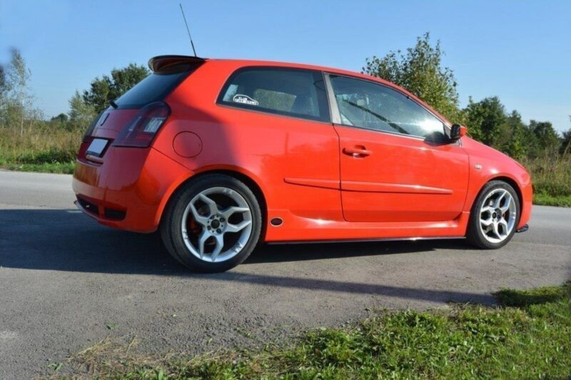 pol_po_SPOILER-CAP-suitable-for-Fiat-STILO-SCHUMACHER-VERSION-1271_4jpg - OPSHOLDERS Red hatchback car parked on a paved road, viewed from the side with a forested background.