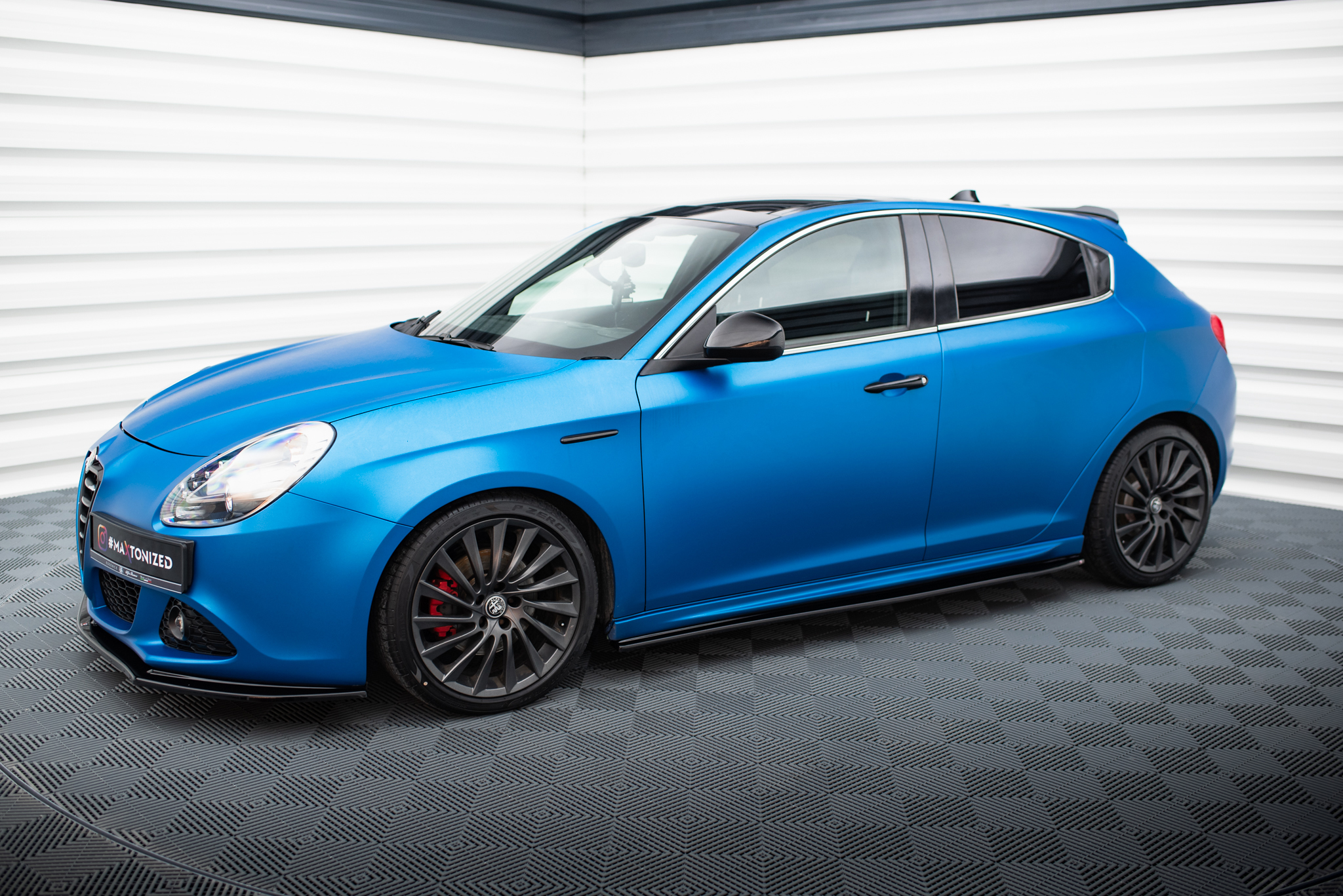 pol_po_Side-Skirts-Diffusers-V-1-suitable-for-Alfa-Romeo-Giulietta-601_3jpg - OPSHOLDERS Blue sports car photographed from the front-left in a bright studio, highlighting its sleek body and large alloy wheels.