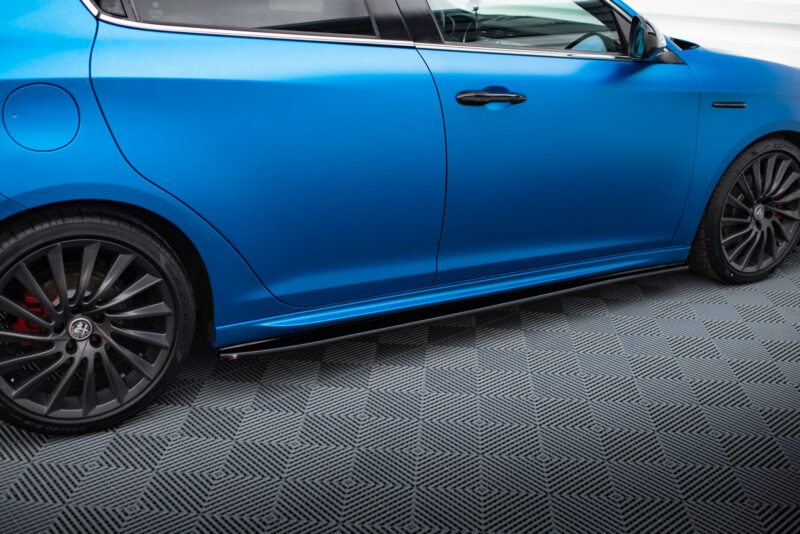 pol_po_Side-Skirts-Diffusers-V-1-suitable-for-Alfa-Romeo-Giulietta-601_4jpg - OPSHOLDERS Close-up of a blue car's side showing the front wheel, alloy rim, brake caliper, door, and side skirt on a checkered floor.