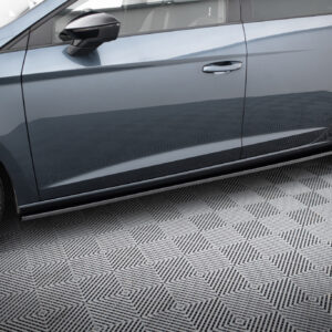 Side of a dark blue-gray car showing doors, mirror, and alloy wheels on a checkered floor.
