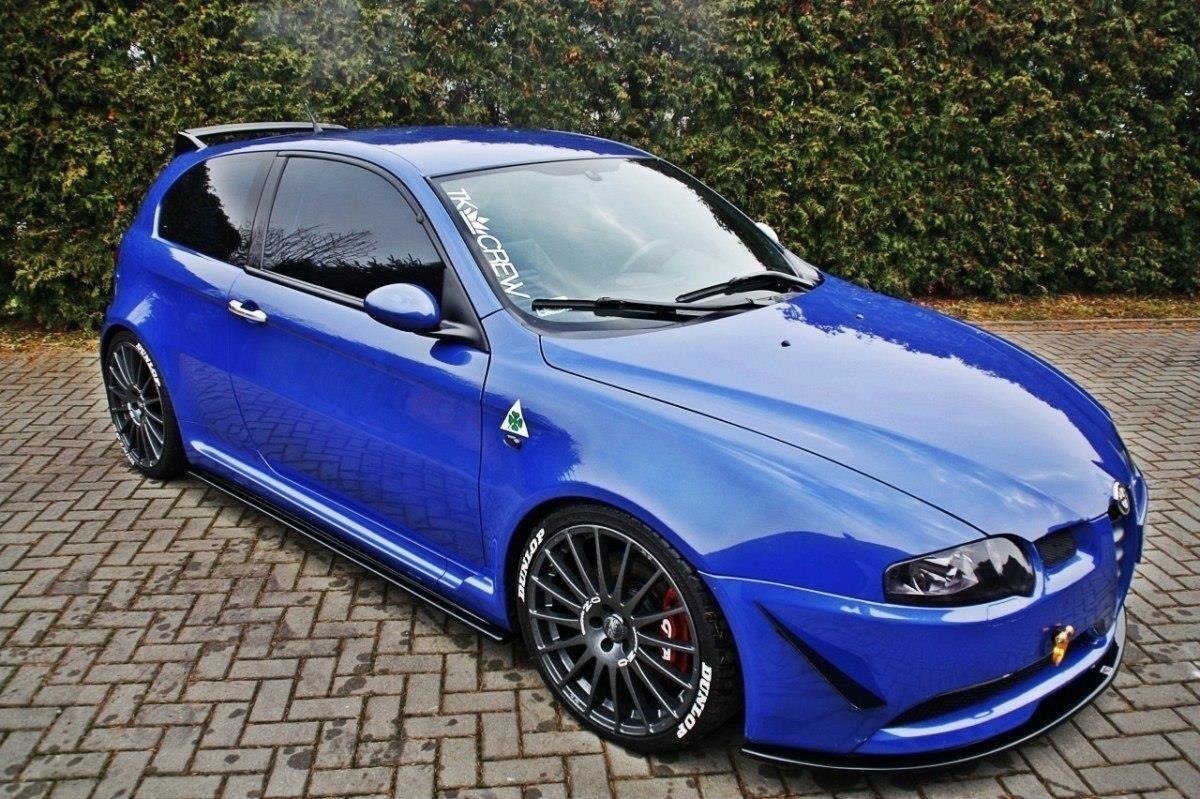 pol_po_Side-Skirts-Diffusers-suitable-for-Alfa-Romeo-147-GTA-76_2jpg - OPSHOLDERS Blue compact sports hatchback with large black aftermarket wheels and low stance, parked on brick driveway, front bumper and roof scoop visible.