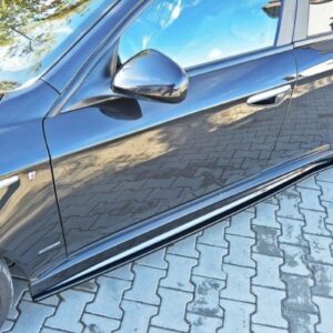 Close-up of a glossy black car's side, showing the front door, mirror, and alloy wheel on a brick-paved surface.