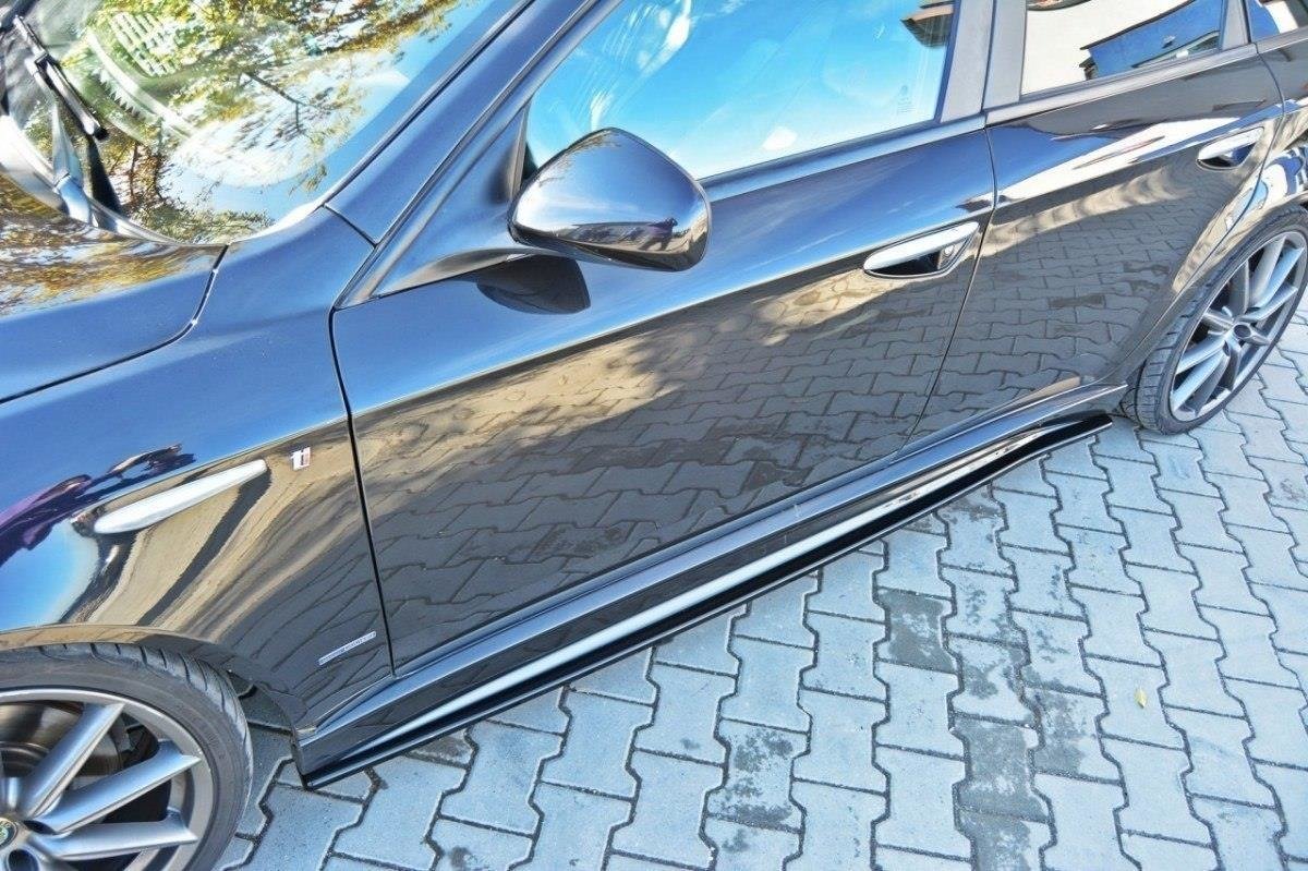 pol_po_Side-Skirts-Diffusers-suitable-for-Alfa-Romeo-159-Ti-77_2jpg - OPSHOLDERS Close-up of a glossy black car's side, showing the front door, mirror, and alloy wheel on a brick-paved surface.