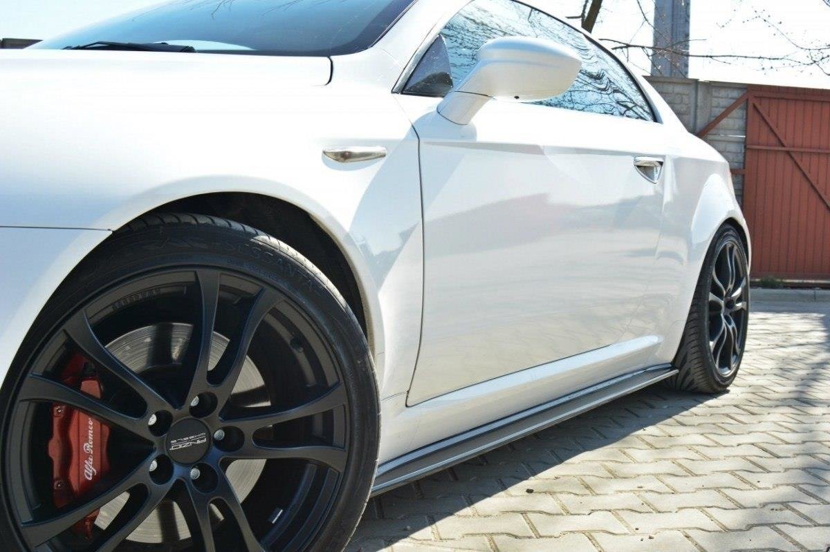 pol_po_Side-Skirts-Diffusers-suitable-for-Alfa-Romeo-Brera-78_3jpg - OPSHOLDERS White sports car side view focusing on the black multi-spoke wheel with red brake caliper on a brick driveway.