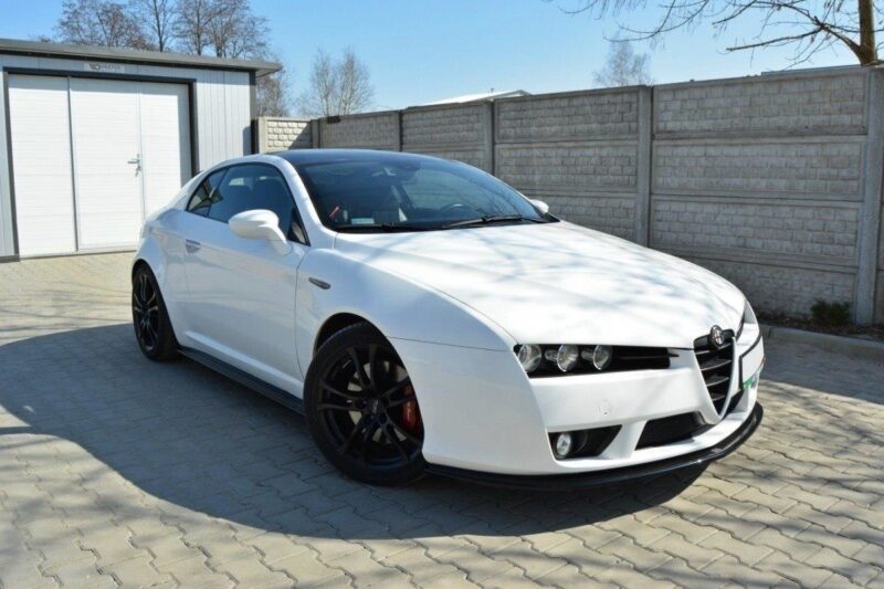 pol_po_Side-Skirts-Diffusers-suitable-for-Alfa-Romeo-Brera-78_4jpg - OPSHOLDERS White Alfa Romeo sports coupe parked on a paved driveway with a storage shed and brick wall in the background; black multi-spoke wheels and red brake calipers visible.