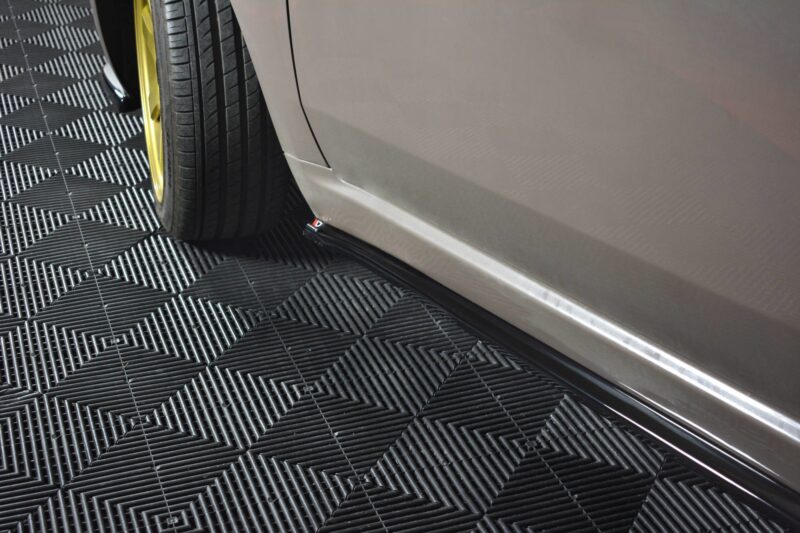 Close-up of a car's front wheel with a bright yellow rim, on a textured dark checkered floor.