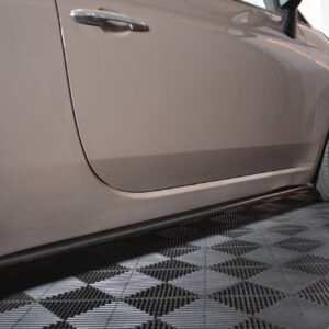 Close-up of a gray car's side panel and gold alloy wheel on a checkered floor.