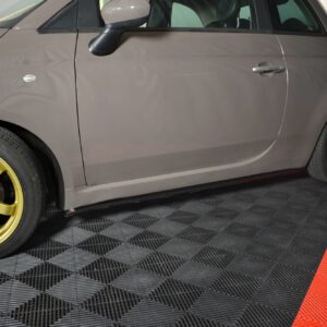 Side view of a gray car with gold alloy wheels parked on a checkered showroom floor.