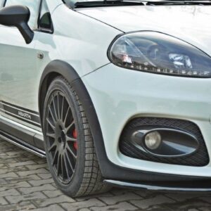 Front-right view of a white Abarth hatchback with black racing stripes, large alloy wheels, and red brake calipers in a driveway setting.