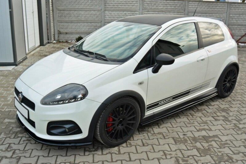 White compact hatchback with black wheels and side stripes labeled Abarth, parked on a brick driveway under a gray fence.