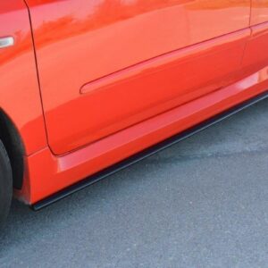 Close-up of a red car's lower side panel and front wheel on asphalt.