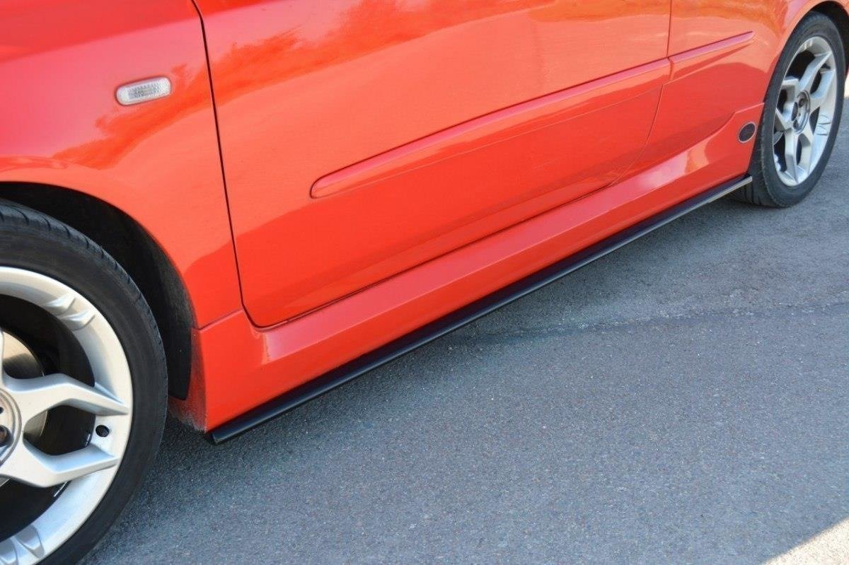 pol_po_Side-Skirts-Diffusers-suitable-for-Fiat-Stilo-Schumacher-2784_2jpg - OPSHOLDERS Close-up of a red car's lower side panel and front wheel on asphalt.