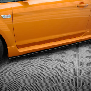 Close-up of an orange car door and front fender showing an 'ST' badge and black alloy wheel on a checkered showroom floor.