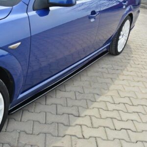 Side view of a blue car with white alloy wheels parked on a light-gray brick driveway, showing the lower body and door handles.