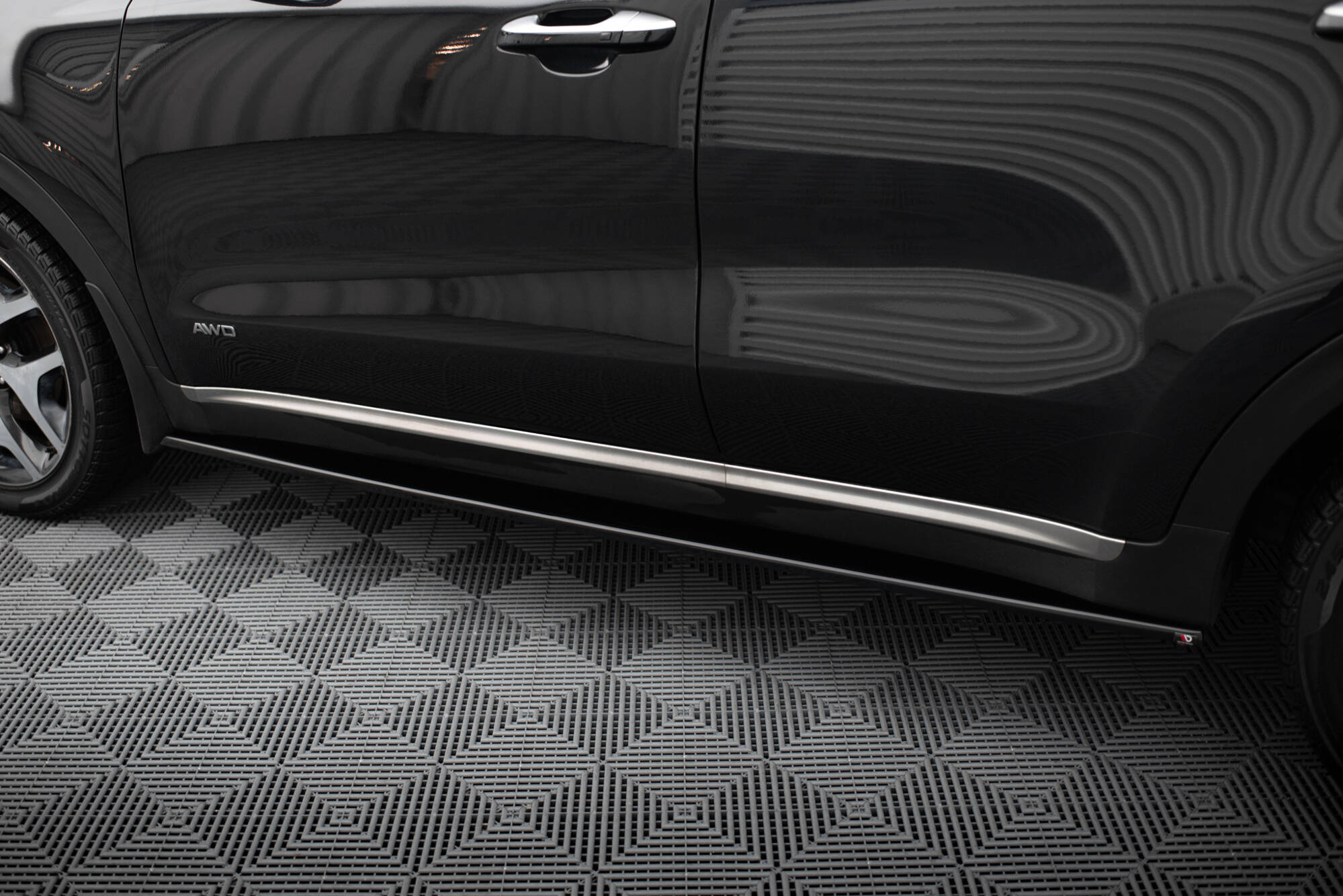 Close-up of a black SUV's side door showing the AWD badge and chrome door handle, with a patterned floor beneath.