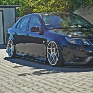 Black sedan with large silver multi-spoke wheels, lowered suspension, parked on a paved driveway beside a garage.