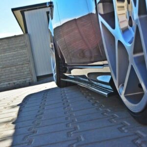 Close-up of a shiny black car with a large silver alloy wheel, parked on a paved driveway with a side skirt visible.