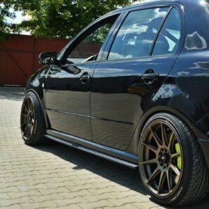 Black sedan with bronze multi-spoke wheels parked on a brick driveway, side view with lowered suspension.