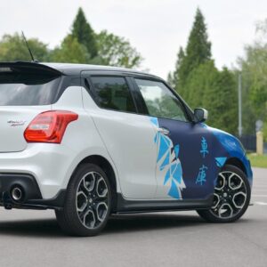 pol_po_Side-Skirts-Diffusers-suitable-for-Suzuki-Swift-Sport-Mk6-8264_2jpg - OPSHOLDERS Rear three-quarter view of a white Suzuki Swift Sport with a blue geometric wrap parked in an empty lot, license plate reads 'MAXTON'