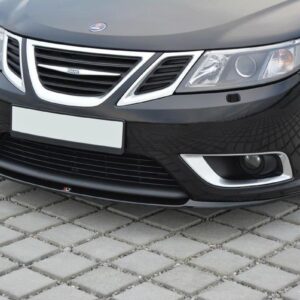 Front view of a black car parked on cobblestones, showing grille, headlights, and lower bumper lip