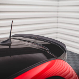 Close-up of a glossy black car roof with a slim antenna and red taillight, indoors by white blinds in the background.