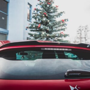 Rear view of a red car with a decorated Christmas tree visible in the background by a building.