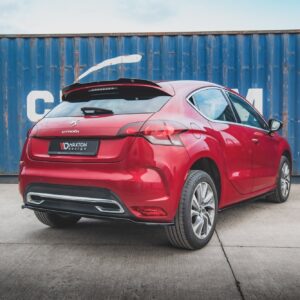Rear three-quarter view of a red Citroën hatchback parked on a concrete lot in front of a weathered blue shipping container.