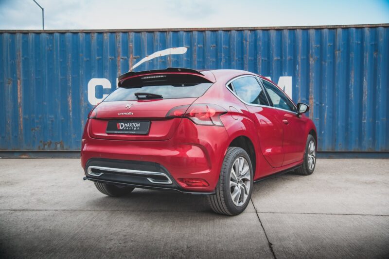Rear three-quarter view of a red Citroën hatchback parked on a concrete lot in front of a weathered blue shipping container.