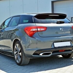 Grey Citroën hatchback viewed from the rear, parked on a paved lot by a light industrial building; dual exhausts and a rear spoiler visible.