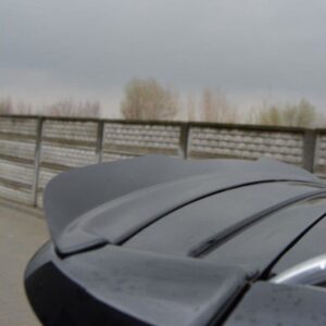 pol_po_Spoiler-Cap-suitable-for-Opel-ZAFIRA-B-OPC-487_4jpg - OPSHOLDERS Close-up of a dark car's rear spoiler on a wet surface, with a railing and cloudy sky in the background of a parking area.