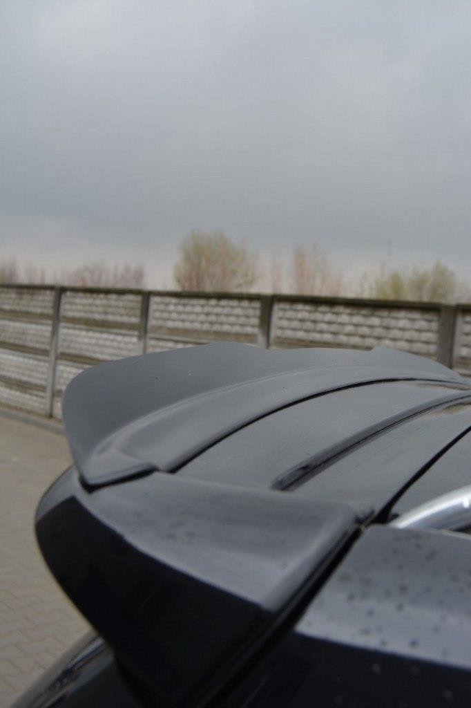 pol_po_Spoiler-Cap-suitable-for-Opel-ZAFIRA-B-OPC-487_4jpg - OPSHOLDERS Close-up of a dark car's rear spoiler on a wet surface, with a railing and cloudy sky in the background of a parking area.