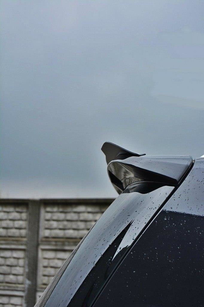 pol_po_Spoiler-Cap-suitable-for-Opel-ZAFIRA-B-OPC-487_6jpg - OPSHOLDERS Close-up of a dark car's glossy rear spoiler with raindrops, set against a cloudy sky and a wooden fence in the background.