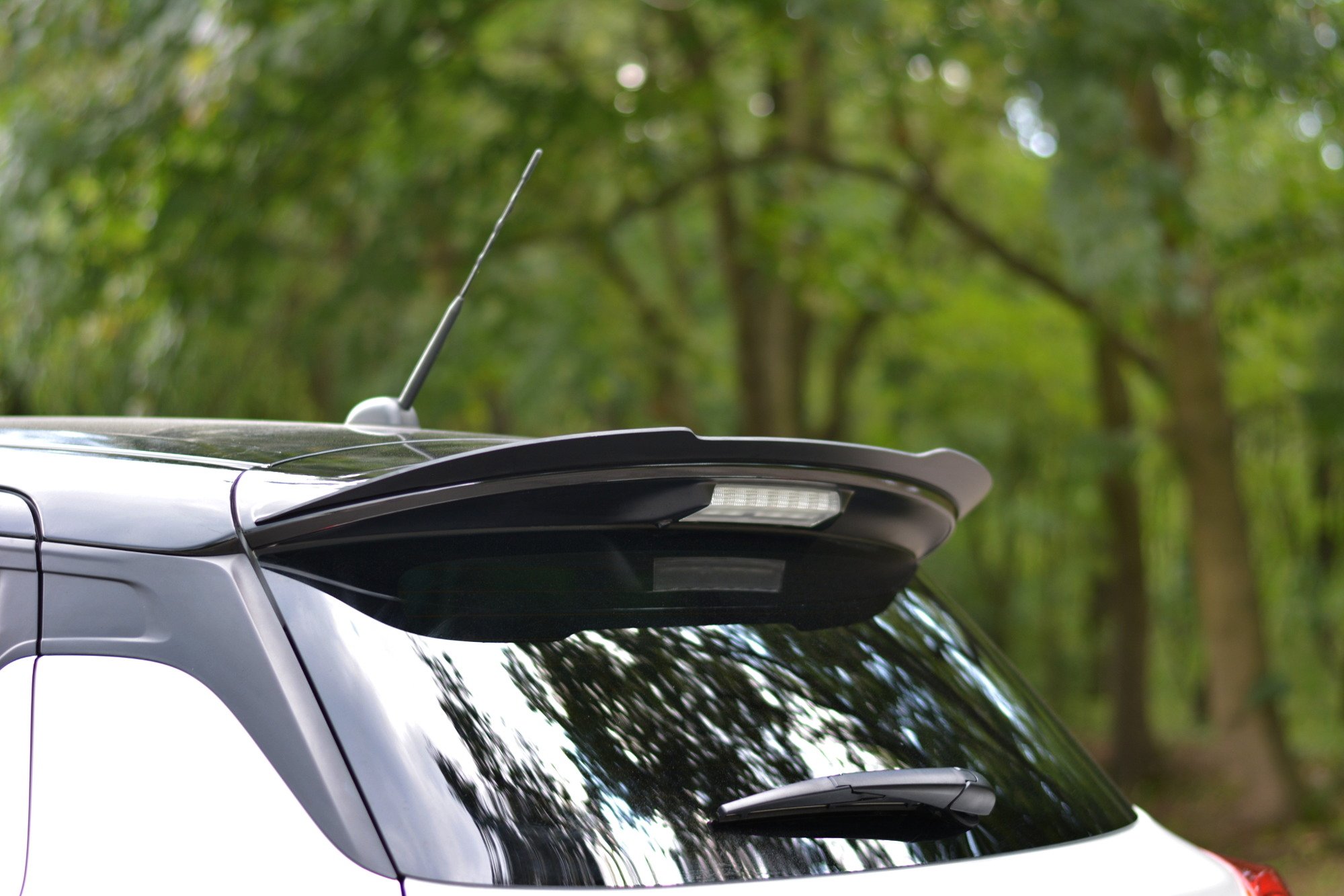 pol_po_Spoiler-Cap-suitable-for-Suzuki-SWIFT-6-SPORT-8255_1jpg - OPSHOLDERS White SUV roof with a tall antenna and blurred green trees in the background.